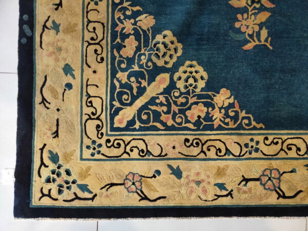 A close view of a dark teal rug with wide borders featuring gold and pink floral motifs.