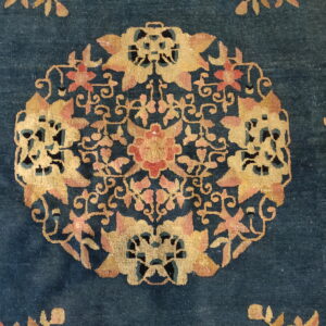 Close-up of a dark blue rug with a detailed gold and pink floral medallion pattern.