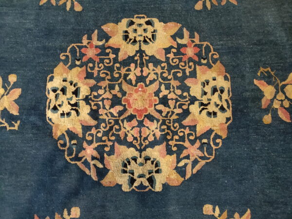 Close-up of a dark blue rug with a detailed gold and pink floral medallion pattern.