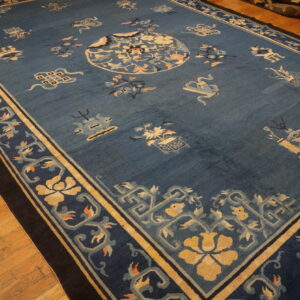 Dusty blue low-pile rug featuring a gold floral medallion and complex borders, displayed on hardwood flooring.