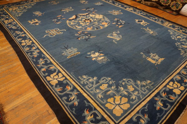 Dusty blue low-pile rug featuring a gold floral medallion and complex borders, displayed on hardwood flooring.