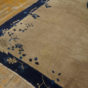Low-pile beige rug with navy blue floral border visible against worn wood flooring.