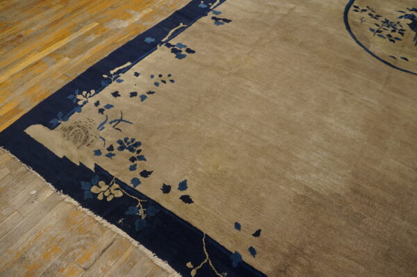 Low-pile beige rug with navy blue floral border visible against worn wood flooring.
