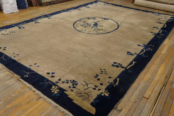 Light brown rug featuring a blue floral border and center bird motif displayed on worn wood floors.