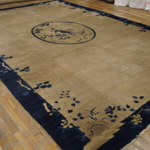 A tan rug with a dark blue border and central bird medallion rests on worn hardwood flooring.