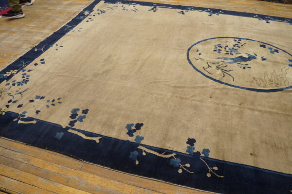 Beige rug featuring a navy blue border with stylized branches and a blue central bird design.