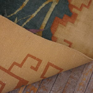 Tan backing with a geometric pattern is visible as the dark green abstract rug is folded on rustic wood planks.