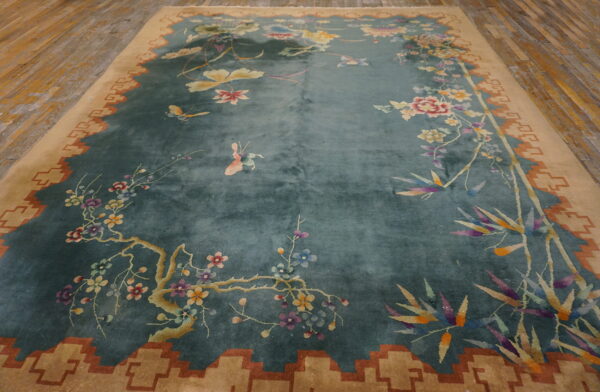 Blue-green floral rug featuring colorful butterflies and a tan geometric border on worn wood flooring.