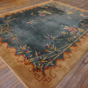 Teal floral rug with a wide camel border featuring a rust key pattern on rustic wood flooring.