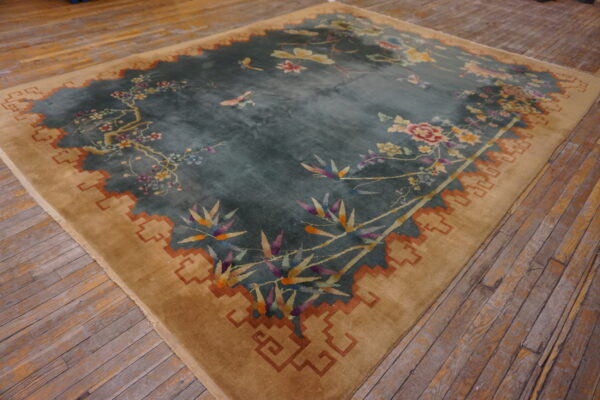 Teal floral rug with a wide camel border featuring a rust key pattern on rustic wood flooring.