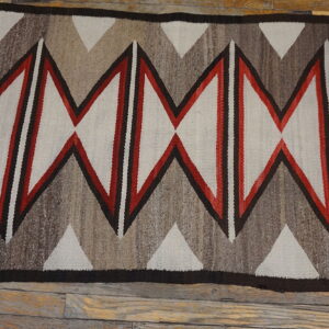 Flat-woven rug featuring bold red, black, and natural gray zigzag diamond patterns on wood planks.
