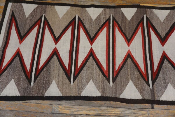 Flat-woven rug featuring bold red, black, and natural gray zigzag diamond patterns on wood planks.