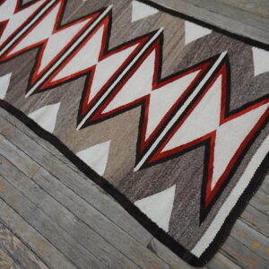 Red, white, and natural tone zigzag rug placed over distressed gray wood flooring.