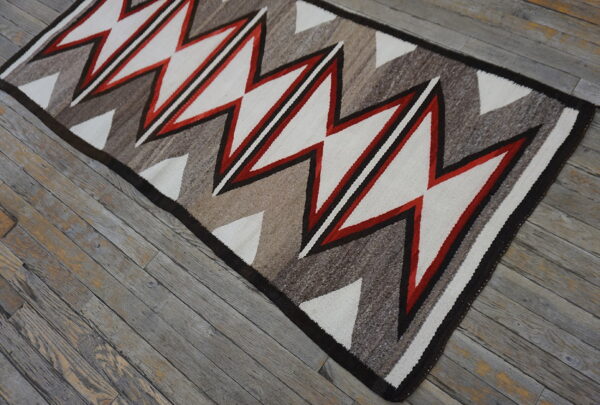 Red, white, and natural tone zigzag rug placed over distressed gray wood flooring.