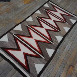 A runner rug with red, white, and brown geometric zigzags rests on worn wood floorboards.