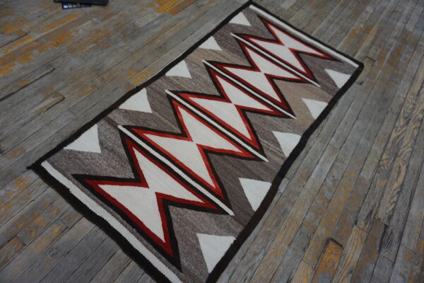 A runner rug with red, white, and brown geometric zigzags rests on worn wood floorboards.