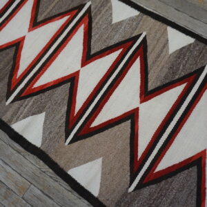 Geometric runner in cream, red, and variegated brown on rustic gray wooden floorboards.