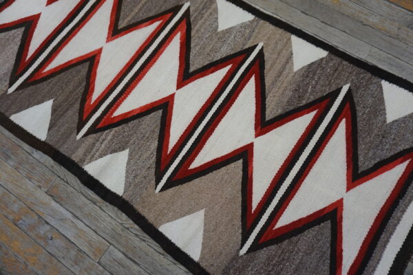 Geometric runner in cream, red, and variegated brown on rustic gray wooden floorboards.