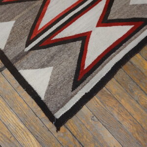 Coarse, flatwoven rug featuring red, cream, and brown geometric patterns rests on rustic wood planks.