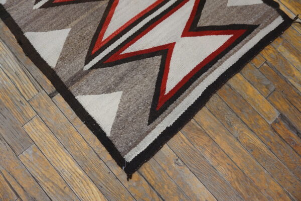 Coarse, flatwoven rug featuring red, cream, and brown geometric patterns rests on rustic wood planks.