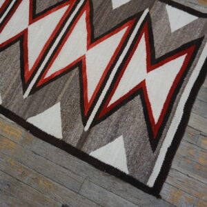 Geometric flatweave rug featuring zigzags in white, red, dark brown, and gray tones over weathered wood.