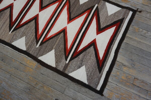 Geometric flatweave rug featuring zigzags in white, red, dark brown, and gray tones over weathered wood.