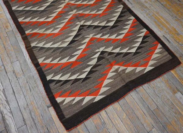 Geometric flatweave rug in earth tones and bright orange on distressed gray wood flooring.