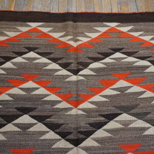 Geometric flatweave rug featuring triangles in orange, cream, and shades of brown, displayed on wood planks.