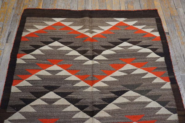 Geometric flatweave rug featuring triangles in orange, cream, and shades of brown, displayed on wood planks.