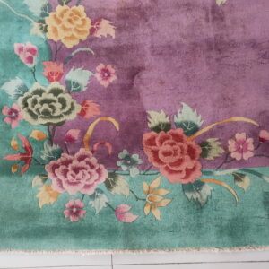 High-pile floral rug with magenta field and teal border resting on a white tiled floor.