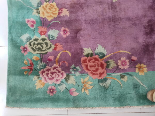 High-pile floral rug with magenta field and teal border resting on a white tiled floor.
