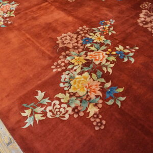 A textured, brick-red rug displays large, colorful pastel floral sprays on light wood plank flooring.