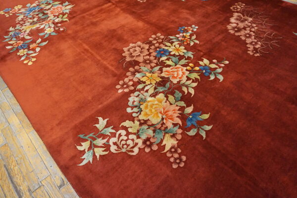 A textured, brick-red rug displays large, colorful pastel floral sprays on light wood plank flooring.
