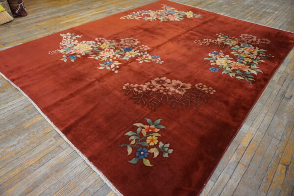 Rust-colored rug with scattered multicolor floral designs sits on aged, gray wooden floorboards.