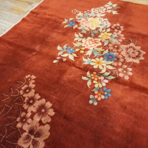 Rust rug with plush pile and colorful floral patterns rests on distressed light wood floors.