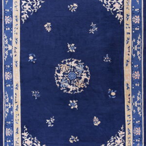 Blue rug with ornate floral patterns, a central medallion, and wide light tan borders.