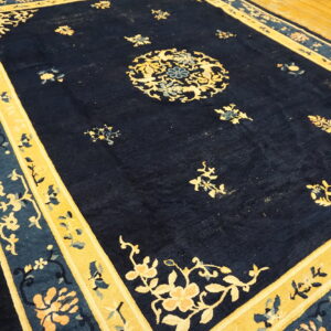 A high-pile navy blue rug with contrasting yellow and pale blue floral medallions and borders on hardwood floor.