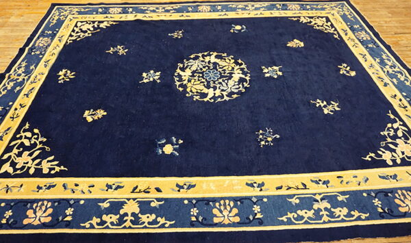 Navy blue rug features a central medallion and ornate gold floral borders on light wood flooring.