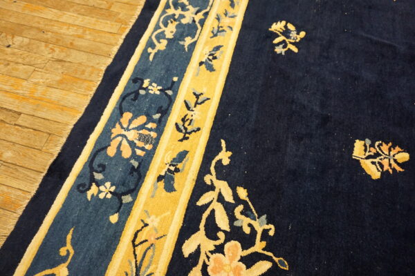 Navy blue rug with gold and teal floral borders rests on light brown hardwood flooring.