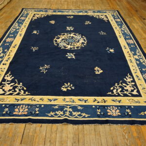 Deep blue floral rug with light yellow and peach borders lying on rustic hardwood floors.