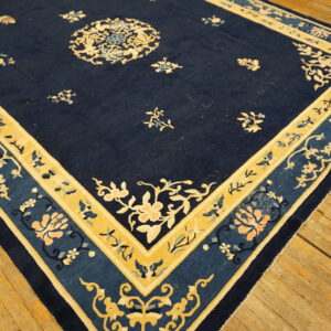 A navy blue rug with gold and pale floral motifs and decorative borders rests on wooden flooring.