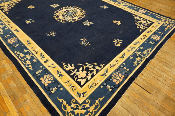 A navy blue rug with gold and pale floral motifs and decorative borders rests on wooden flooring.