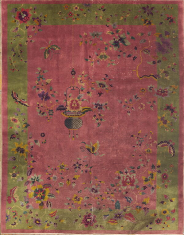 Pink field rug with an olive green border and intricate floral, butterfly, and hanging basket designs.