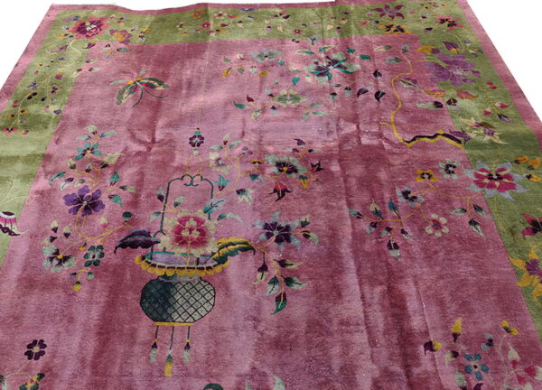 Rose-colored, high-sheen rug with an olive green border and a decorative vase and floral pattern.