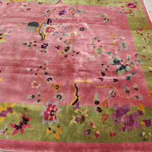 Ornate dusty rose rug with a green border featuring detailed floral vines and butterflies on cement flooring.