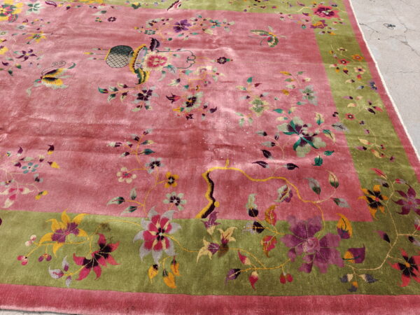 Ornate dusty rose rug with a green border featuring detailed floral vines and butterflies on cement flooring.