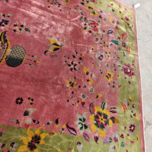 Plush rose pink rug featuring a vibrant floral pattern and olive green border on concrete flooring.