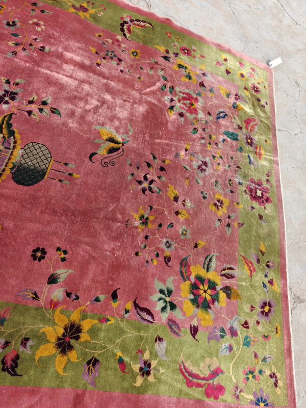 Plush rose pink rug featuring a vibrant floral pattern and olive green border on concrete flooring.