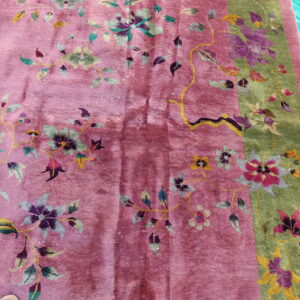 Close view of a rose and sage floral rug resting on a blue tarp near a tan shoe.