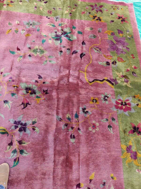 Close view of a rose and sage floral rug resting on a blue tarp near a tan shoe.